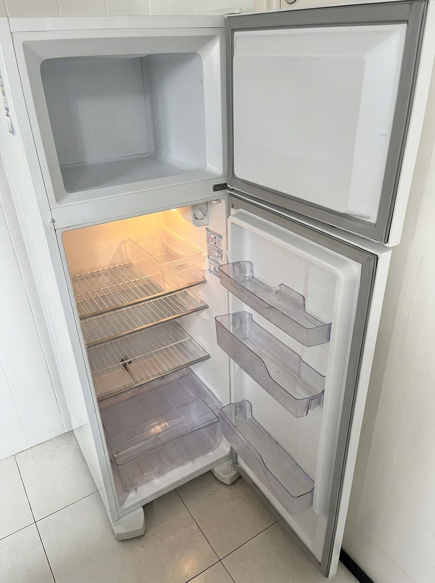 Interior da geladeira com as duas portas abertas e vazia, mostrando as prateleiras aramadas, a gaveta transparente de frutas e legumes e os nichos da porta.