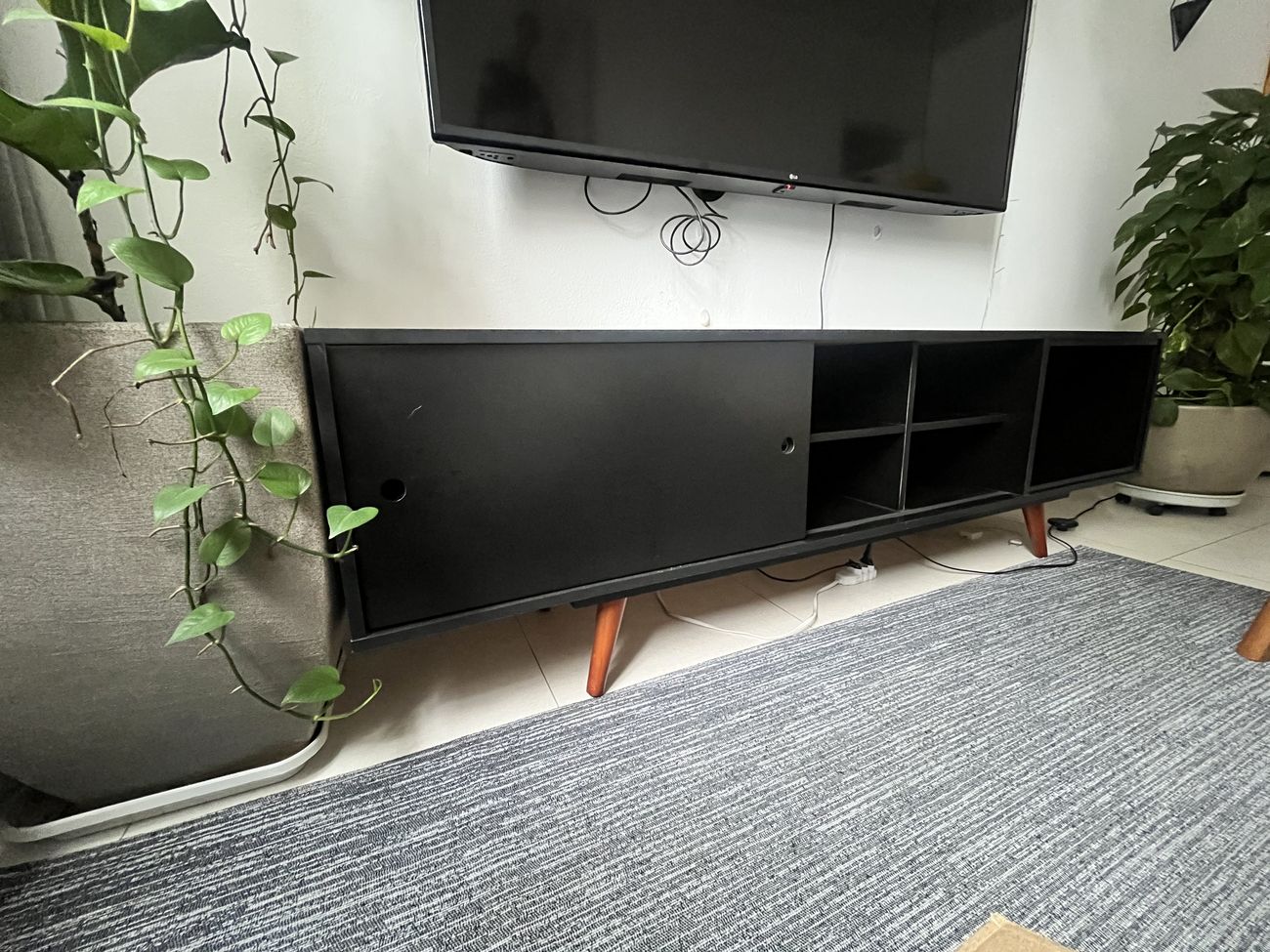 Rack de TV preto e baixo, visto de três quartos, com porta de correr fechada à esquerda e nichos abertos à direita.
