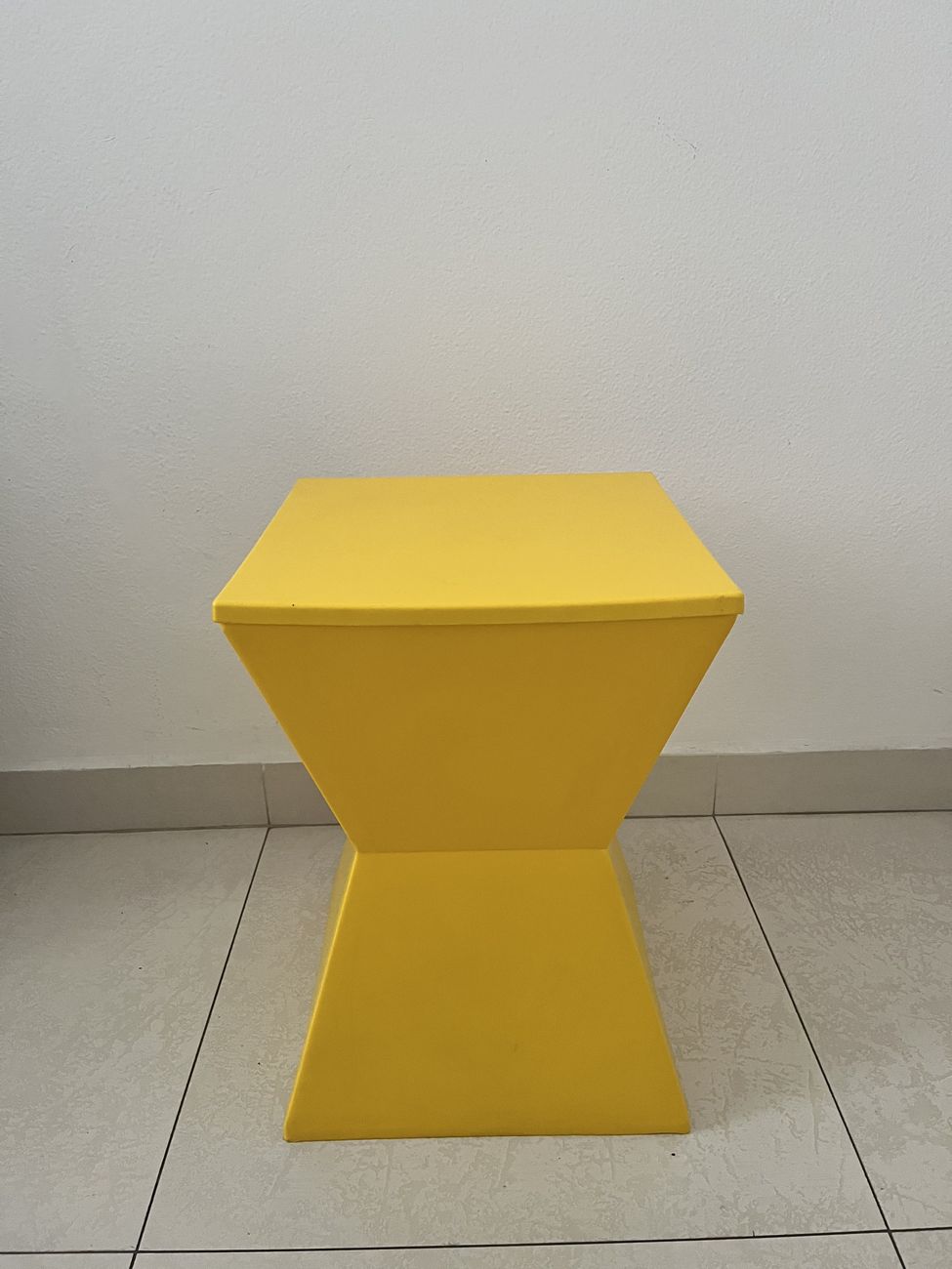 A mesma banqueta amarela vista de frente, mostrando a simetria dos dois troncos de pirâmide.