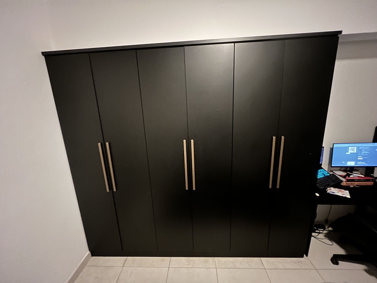 Guarda-roupa preto de seis portas visto de frente, ocupando a parede inteira do quarto, com puxadores verticais escovados.