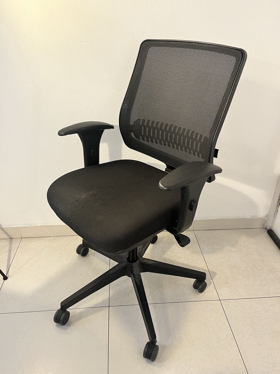 Cadeira de escritório preta com encosto em tela mesh, assento estofado e base de cinco rodízios.