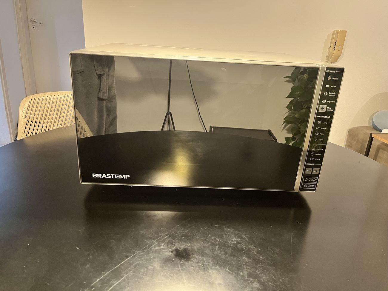 Micro-ondas Brastemp de porta espelhada visto de frente, sobre uma mesa preta.