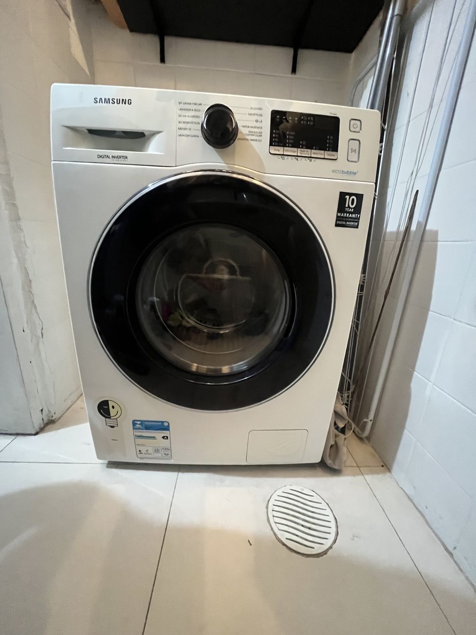 Lava e seca Samsung branca vista de frente, instalada na área de serviço, com o painel no topo e a porta redonda de vidro.