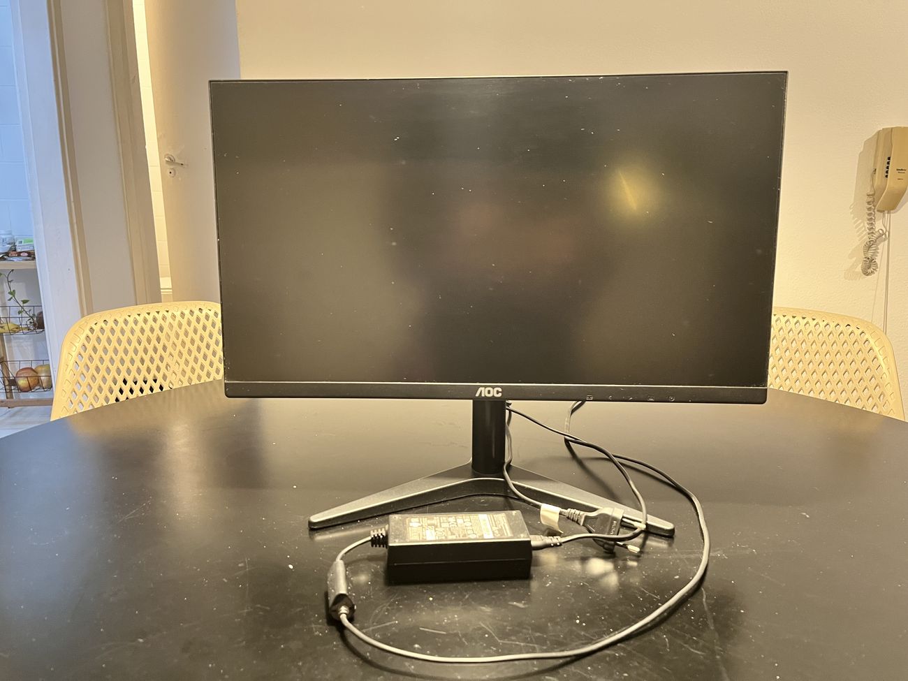 Monitor AOC de 21,5 polegadas visto de frente, sobre uma mesa preta, com a fonte e o cabo ao lado.