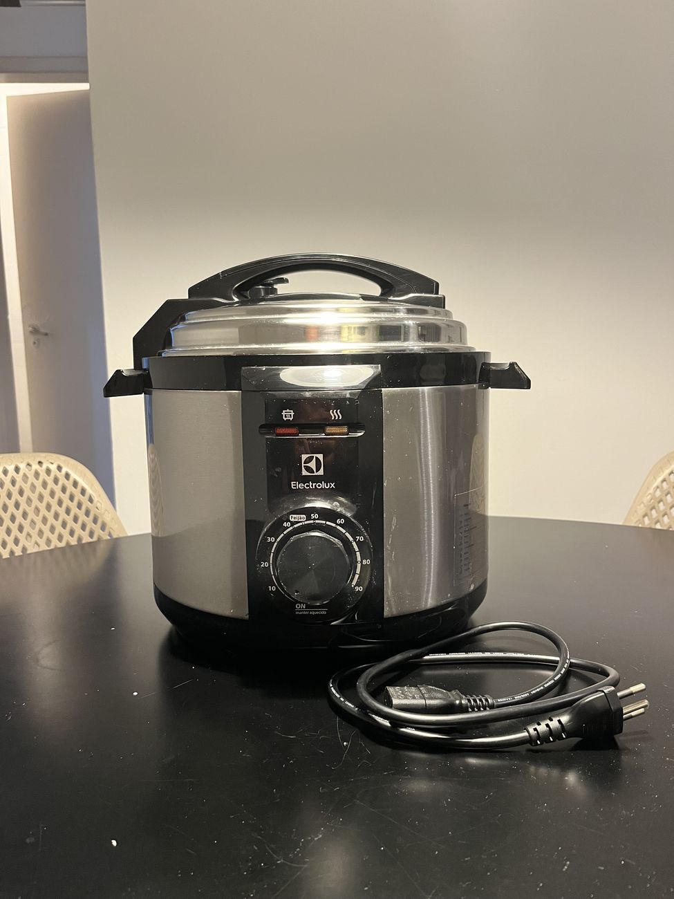 Panela de pressão elétrica Electrolux em inox escovado e preto, vista de frente, com o timer rotativo e o cabo removível ao lado.