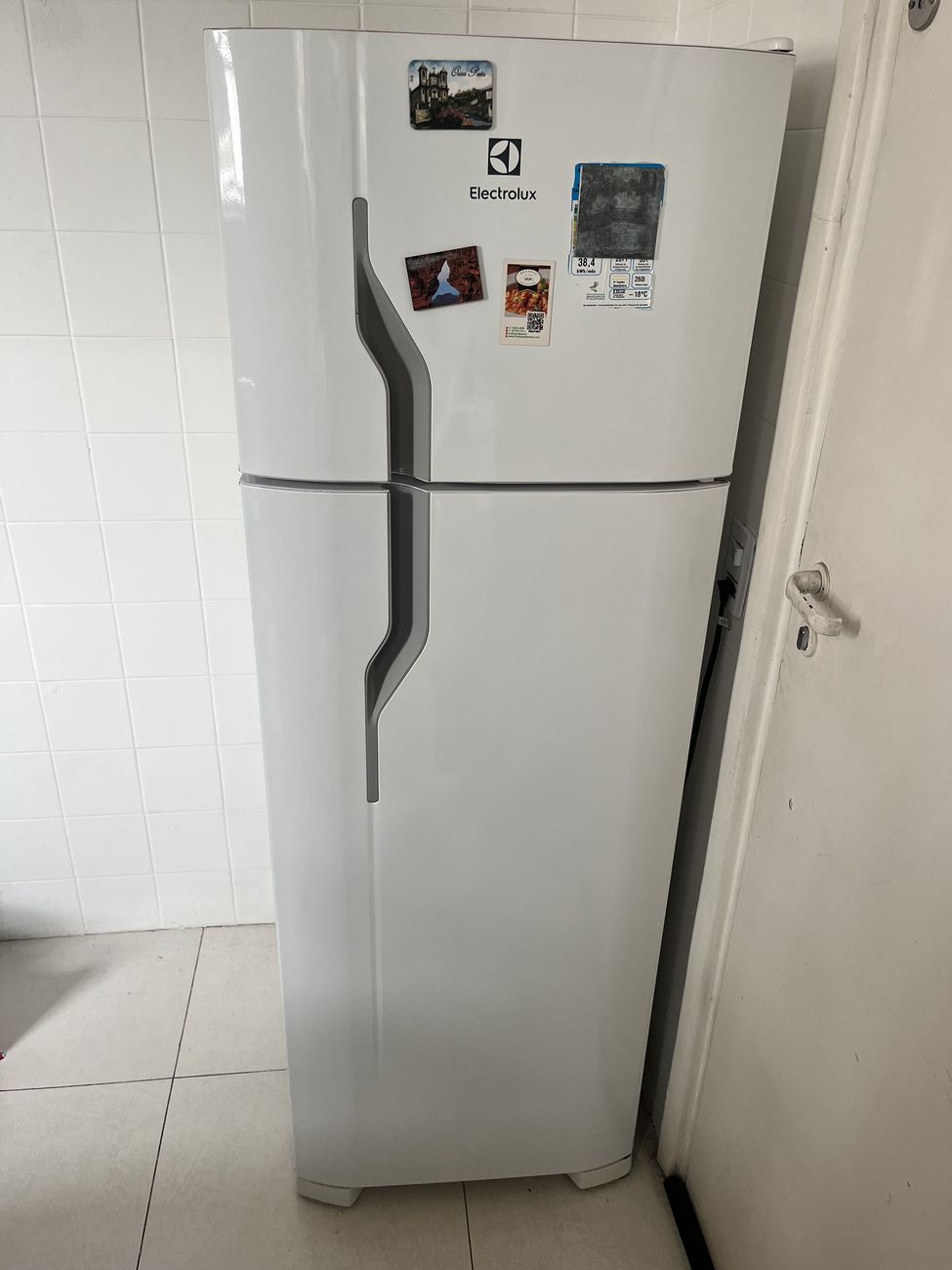 Geladeira Electrolux branca de duas portas vista de frente, fechada, ao lado da porta da área de serviço.