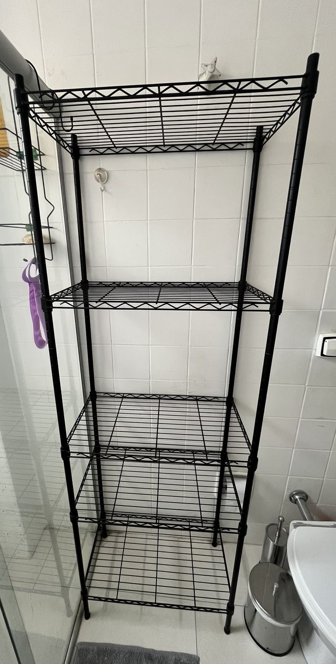 Estante aramada preta de cinco prateleiras, vazia, montada contra uma parede de azulejo branco.