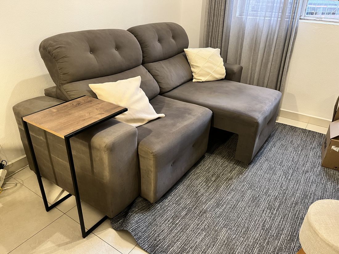 Sofá na sala, sobre o tapete cinza, com a mesa lateral em C ao lado.