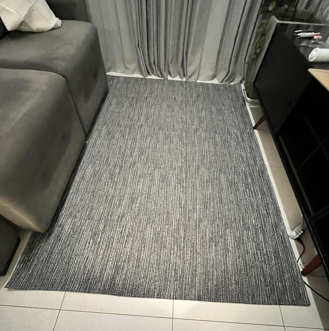 Tapete cinza riscadinho estendido na sala, entre o sofá e o rack, sobre o piso claro.