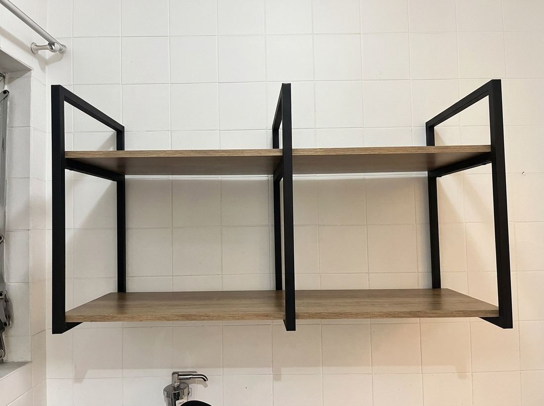 Nicho aéreo de duas prateleiras de madeira com estrutura de metal preto, vazio, fixado na parede de azulejo branco da cozinha.